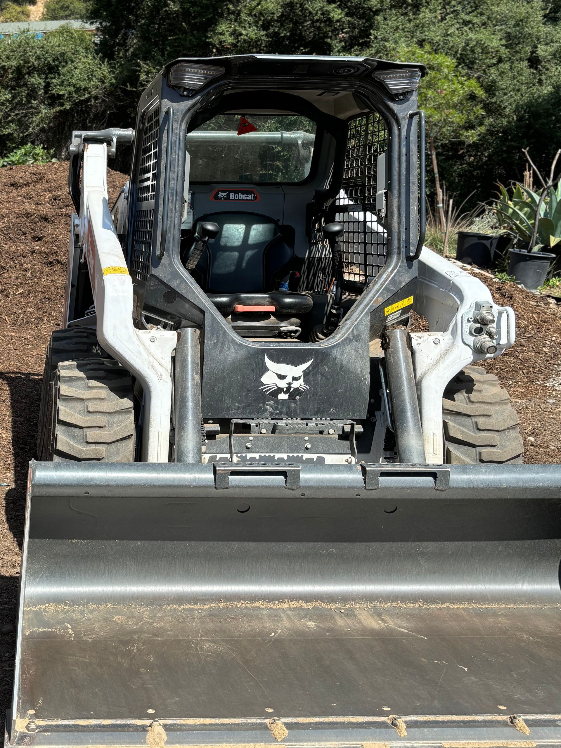 A bobcat skid steer is sitting on top of a pile of mulch.