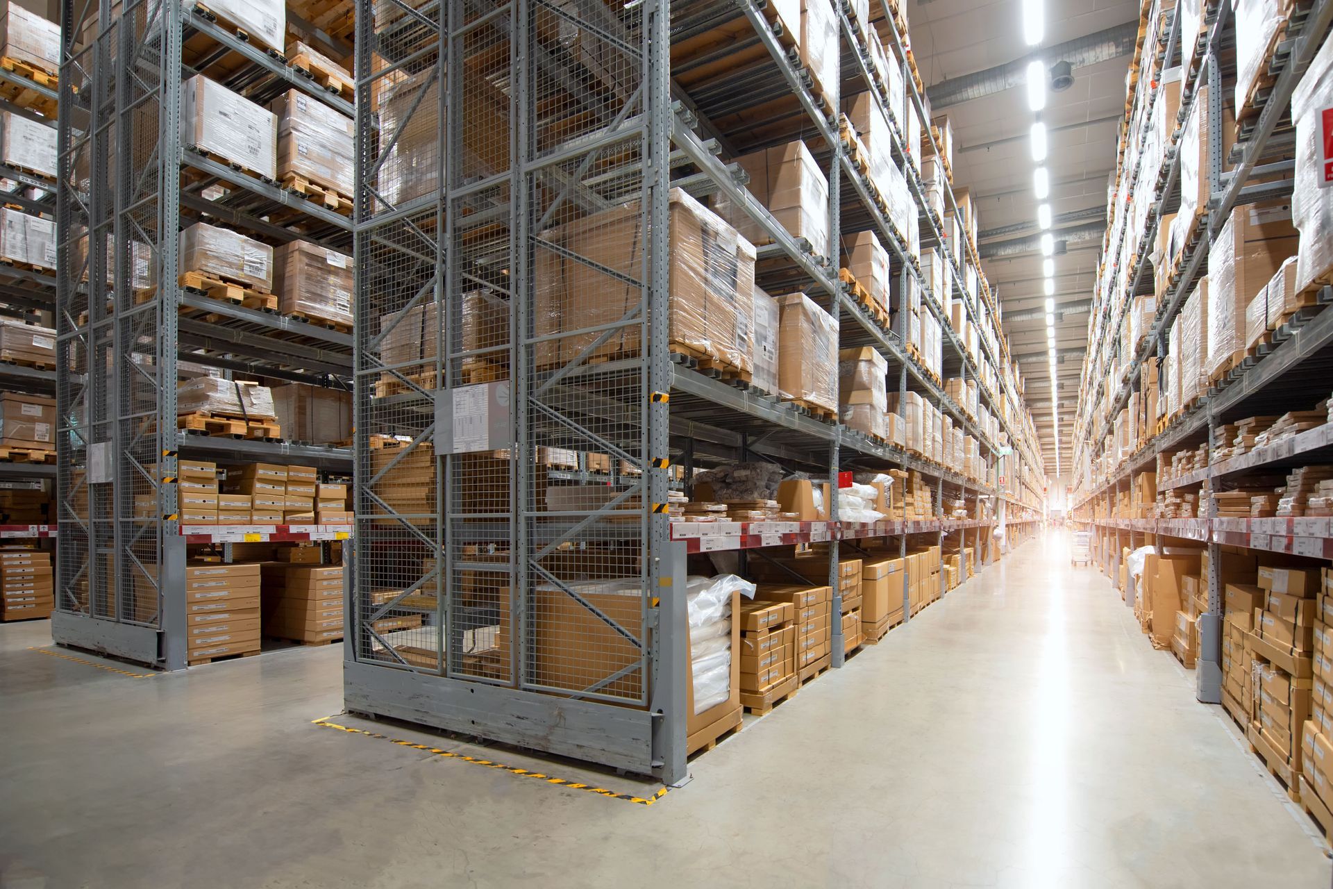 Warehouse aisle with tall storage racks, stacked boxes, and bright overhead lighting