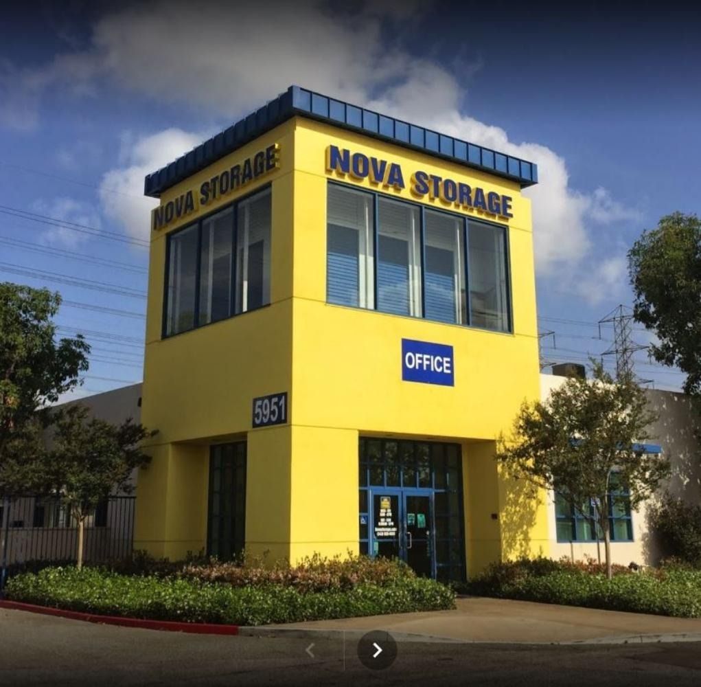 Yellow Nova Storage building with blue trim, "Office" sign, blue door, and small landscaping in front.