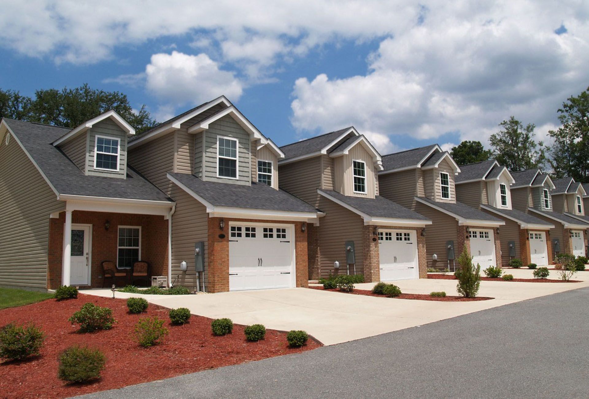 Row of modern suburban houses with garages and landscaped front yards under a partly cloudy sky