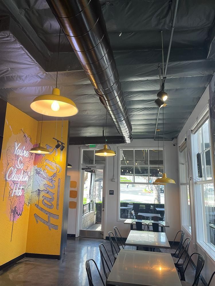 An interior view of a cafe with yellow walls, industrial-style ceiling, pendant lights, and tables with chairs.