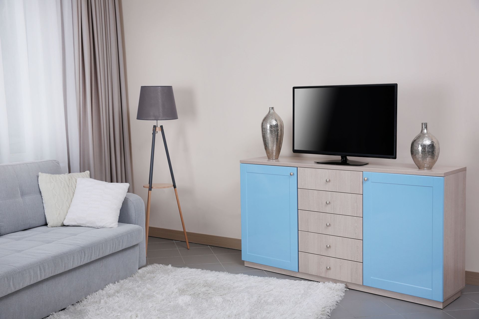 Modern living room with gray sofa, floor lamp, TV, and blue cabinet on a white rug