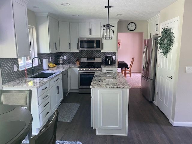 A kitchen with white cabinets , granite counter tops , stainless steel appliances and a large island.