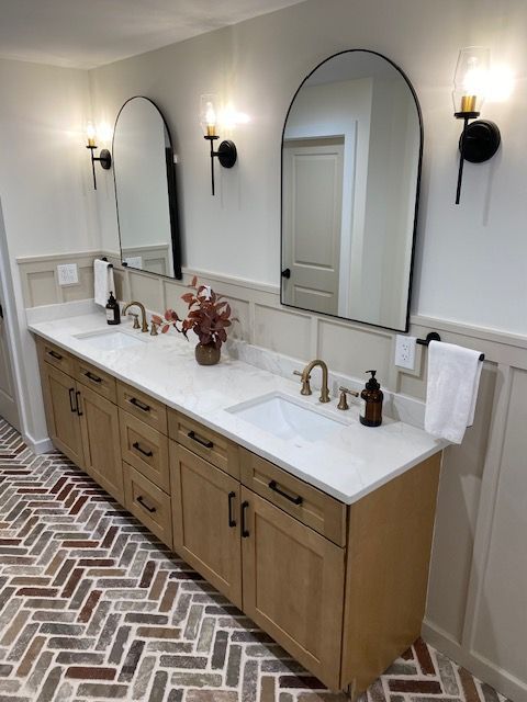 A bathroom with two sinks , two mirrors and a brick floor.