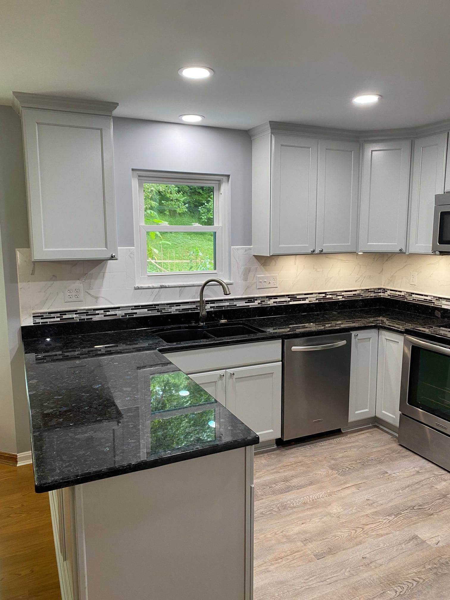 A kitchen with white cabinets, black counter tops, stainless steel appliances, and a window.