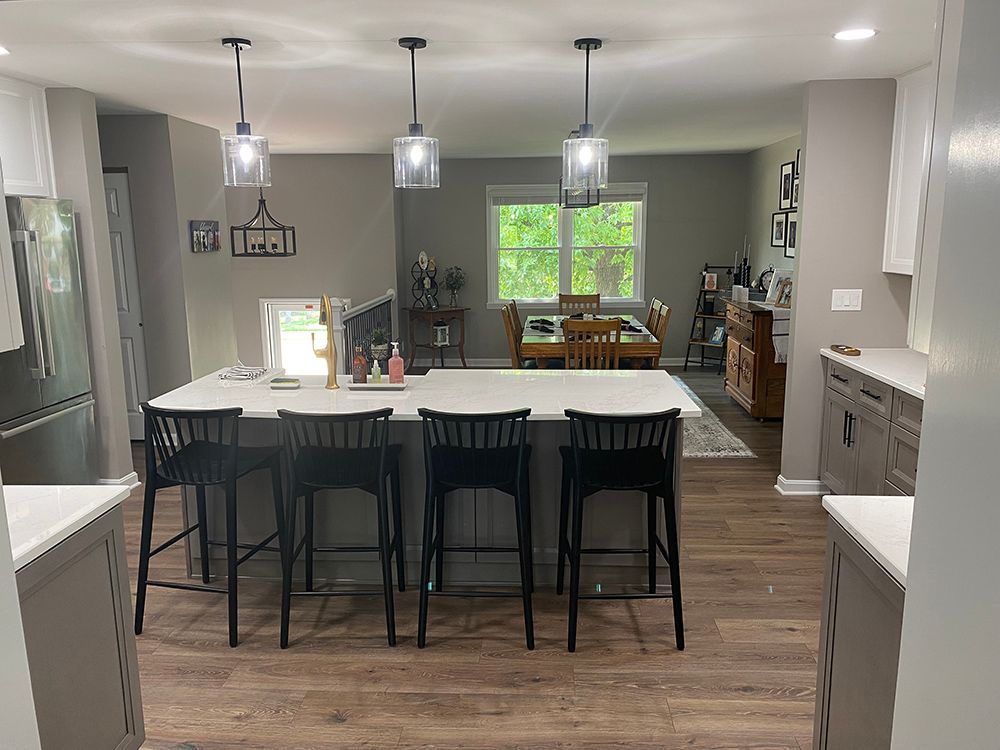 A kitchen with a large island and stools and a dining room in the background