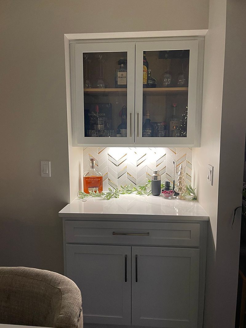 A kitchen with white cabinets and glass doors filled with bottles and glasses