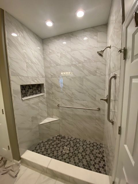 A bathroom with a walk in shower with a glass door and marble walls