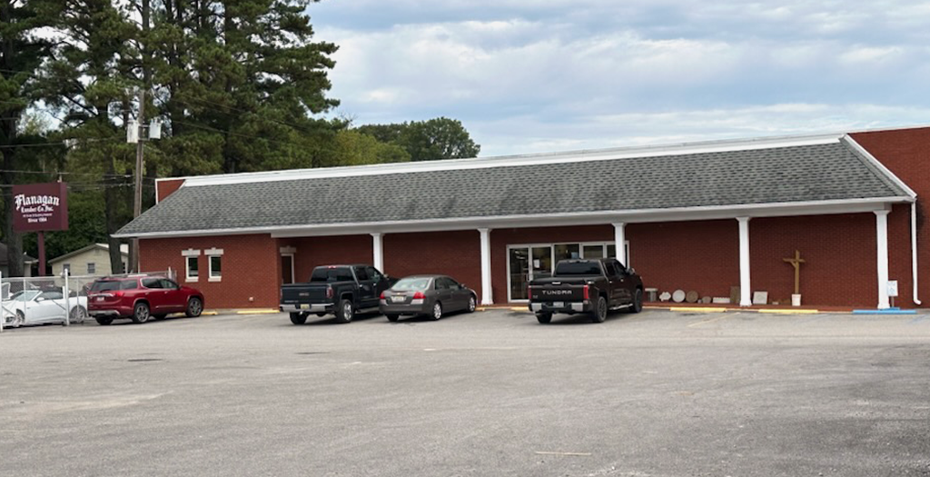 A row of cars are parked in front of a large red building.
