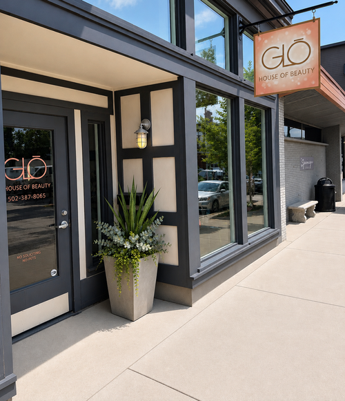 Storefront with large windows and a hanging “Glo” sign on a sunny sidewalk.