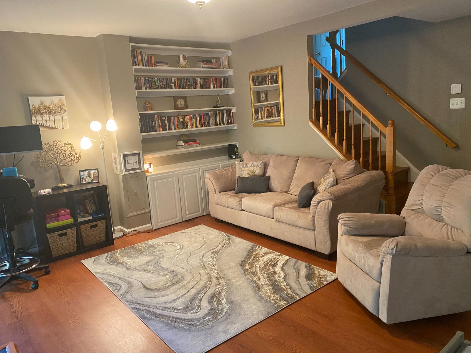 A living room with a couch, chair, rug and stairs.