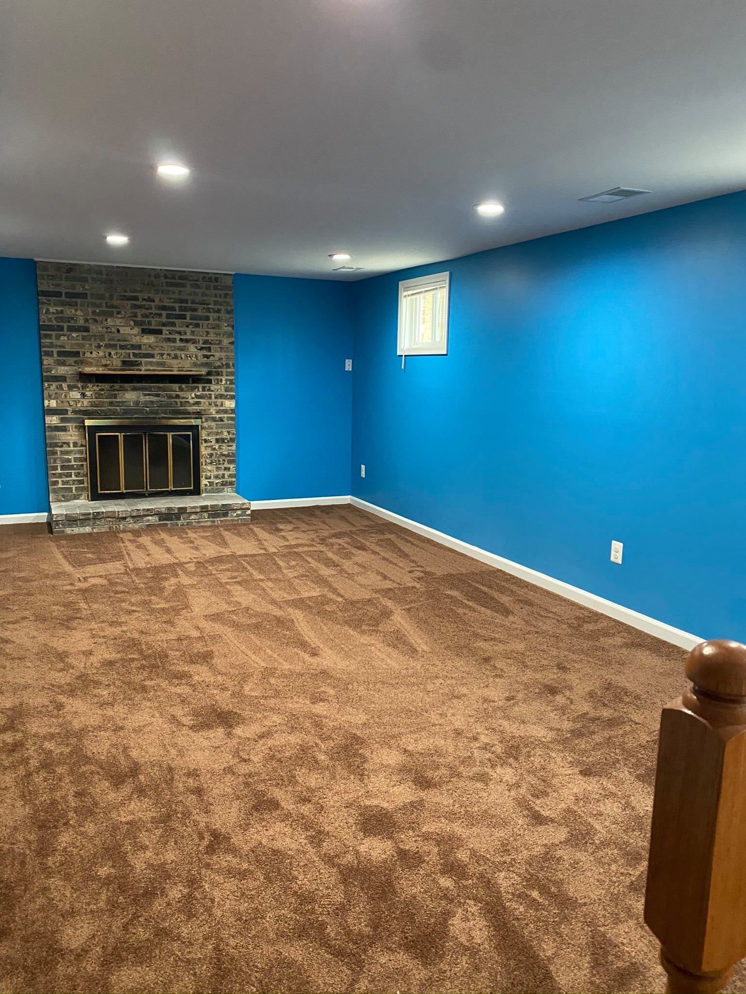 An empty basement with blue walls and a fireplace.