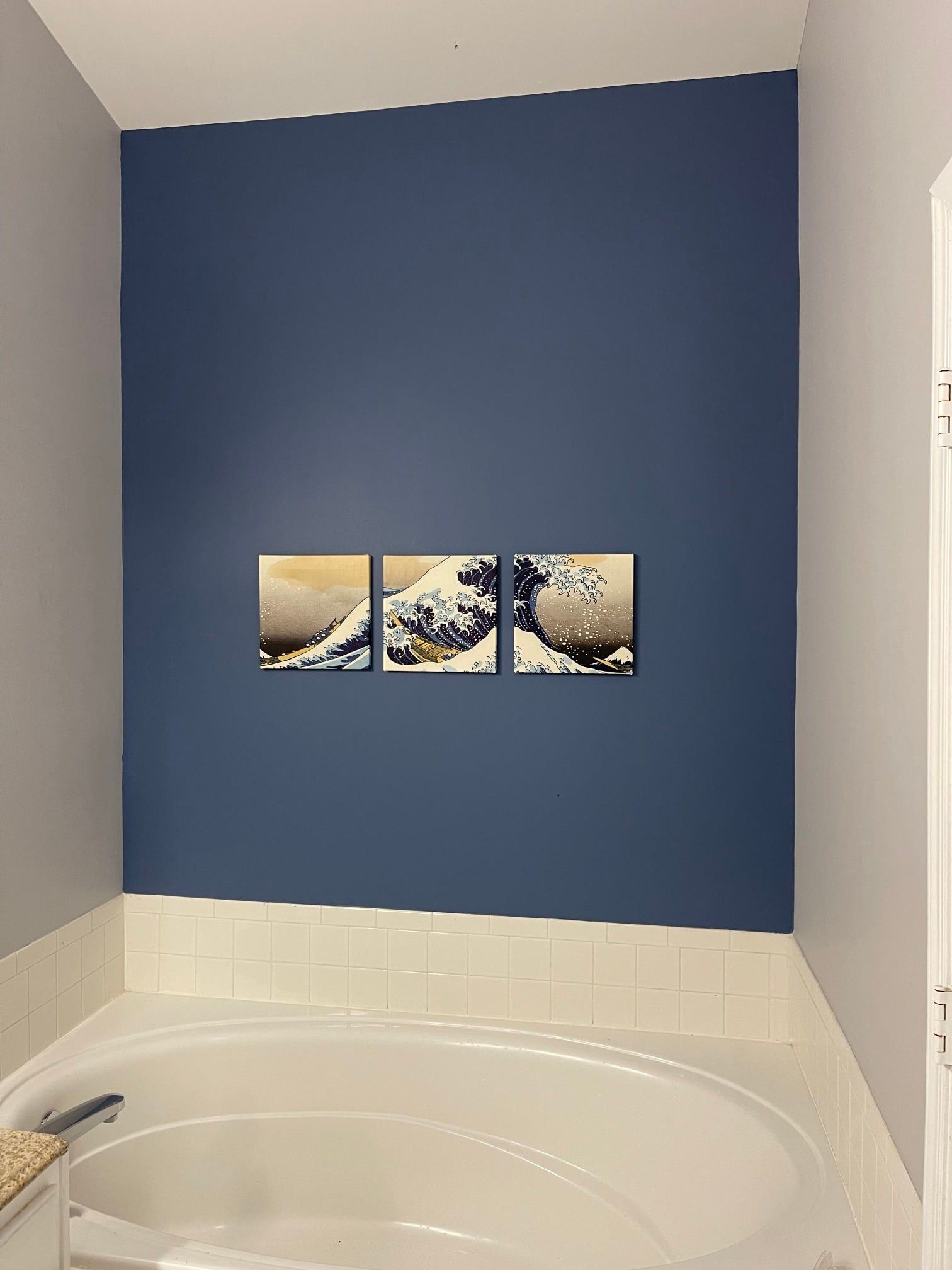 A bathroom with a bathtub and three paintings on the wall.