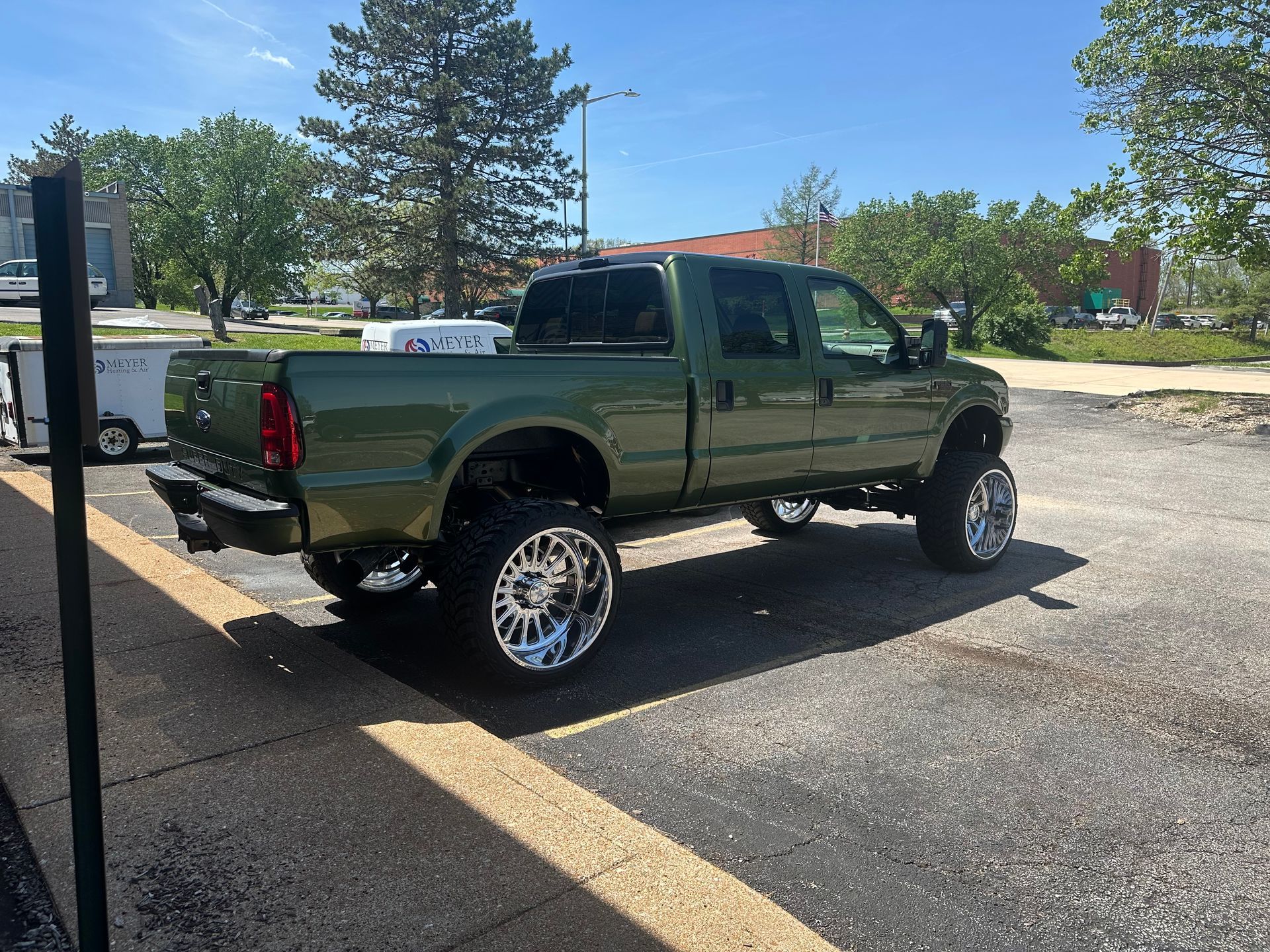 Olive green lifted pickup truck with large chrome wheels parked outside.