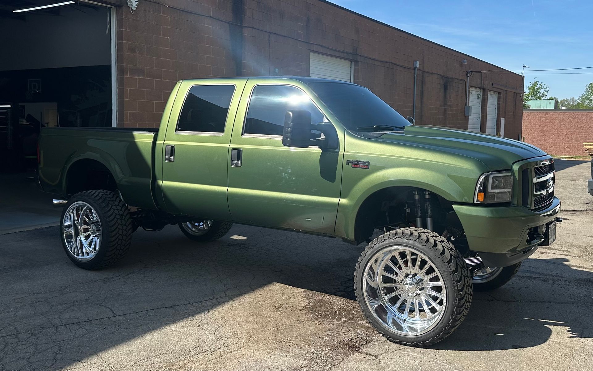 Olive green lifted truck with chrome wheels parked near a building.