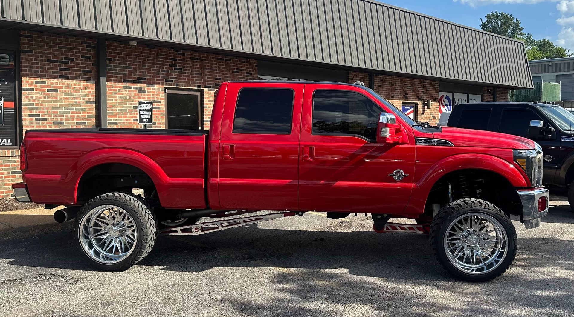 Red lifted pickup truck parked outside a building, shiny chrome wheels.