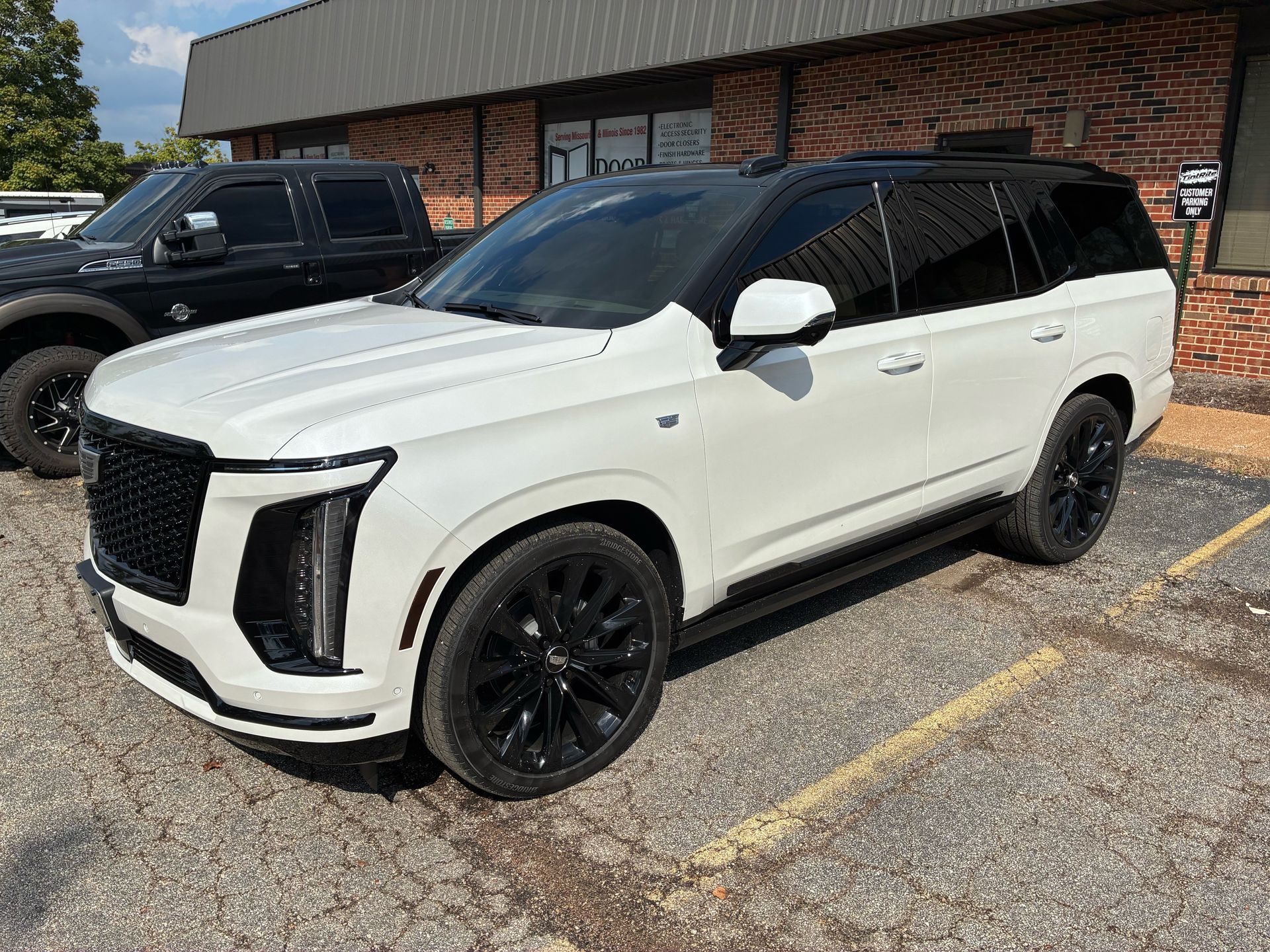 White Cadillac Escalade SUV with black accents parked outside a brick building.