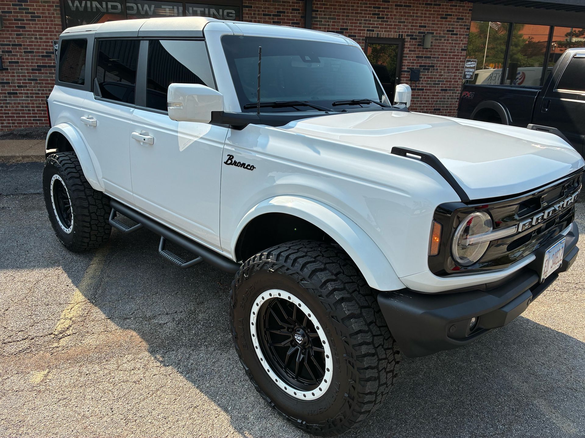 White Ford Bronco SUV with black wheels, parked near a building.