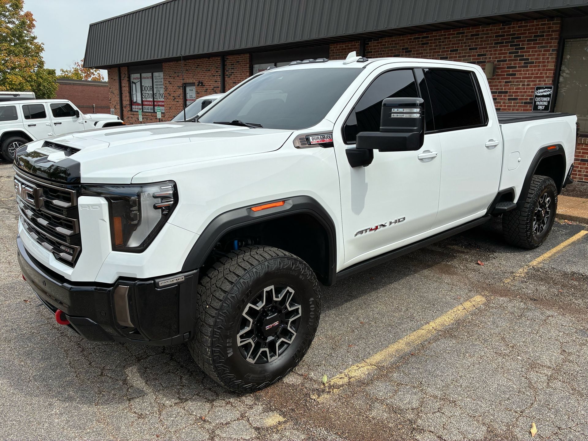 White GMC truck parked outside a building. Dark tinted windows, black wheels, and a red tow hook.