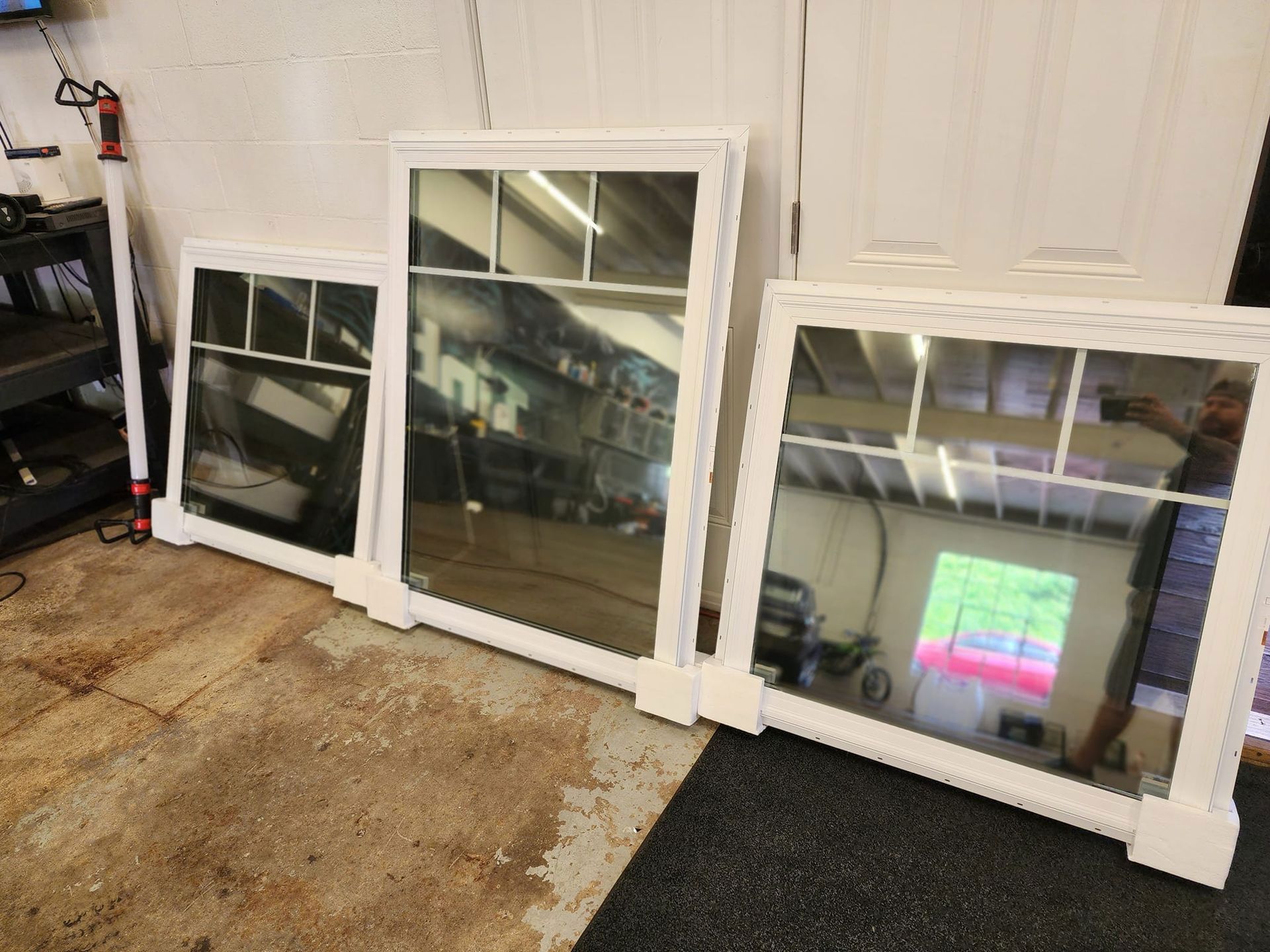 Three white-framed mirrors leaning against a white wall; they vary in size.