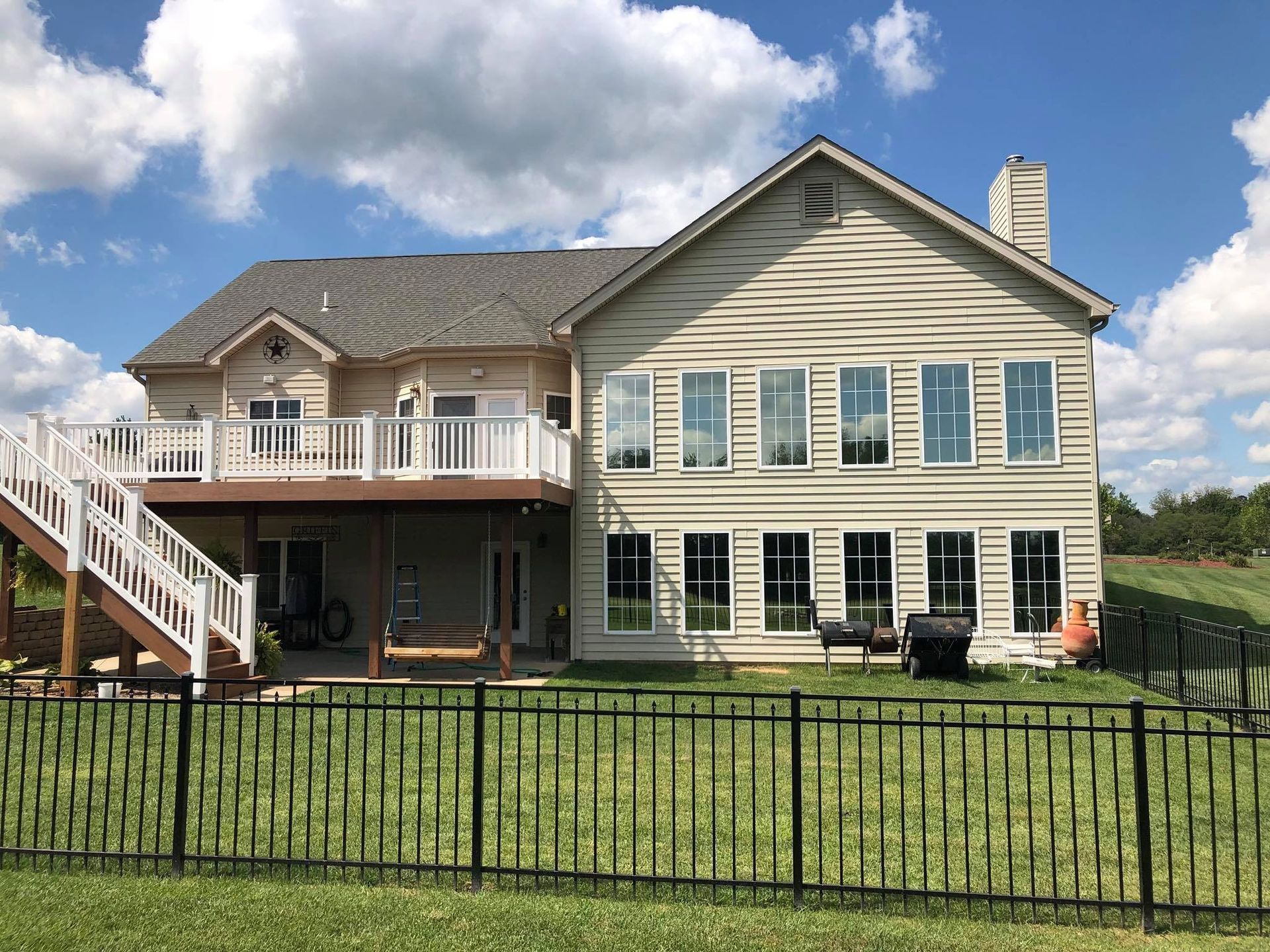 Back of a two-story beige house with a deck, black fence, and blue sky with clouds.