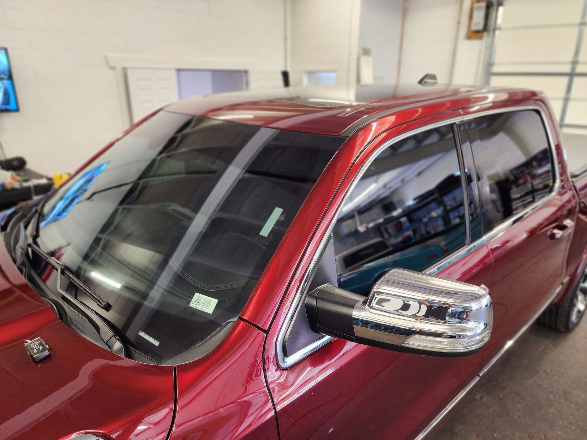 Red pickup truck with tinted windows, parked indoors. Chrome side mirror reflects nearby shop items.