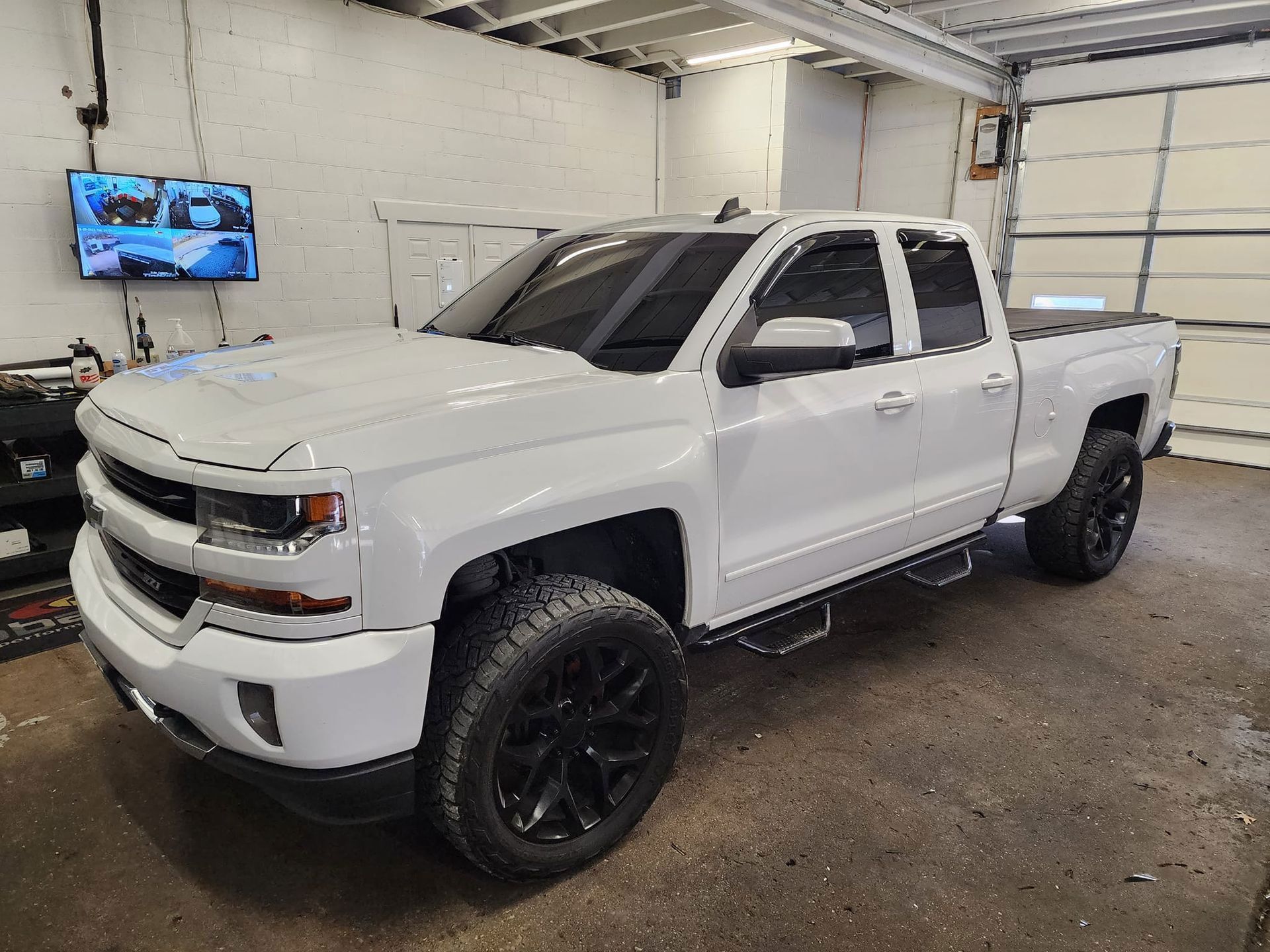 White Chevy pickup truck with black wheels and tinted windows in a garage.