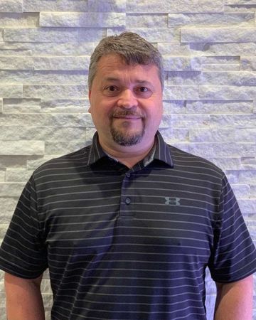 A man in a black striped shirt is standing in front of a brick wall.