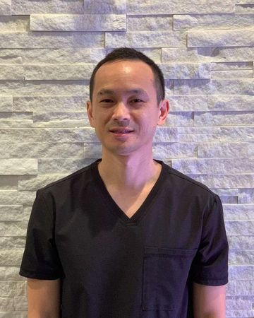 A man in a black scrub top is standing in front of a stone wall.