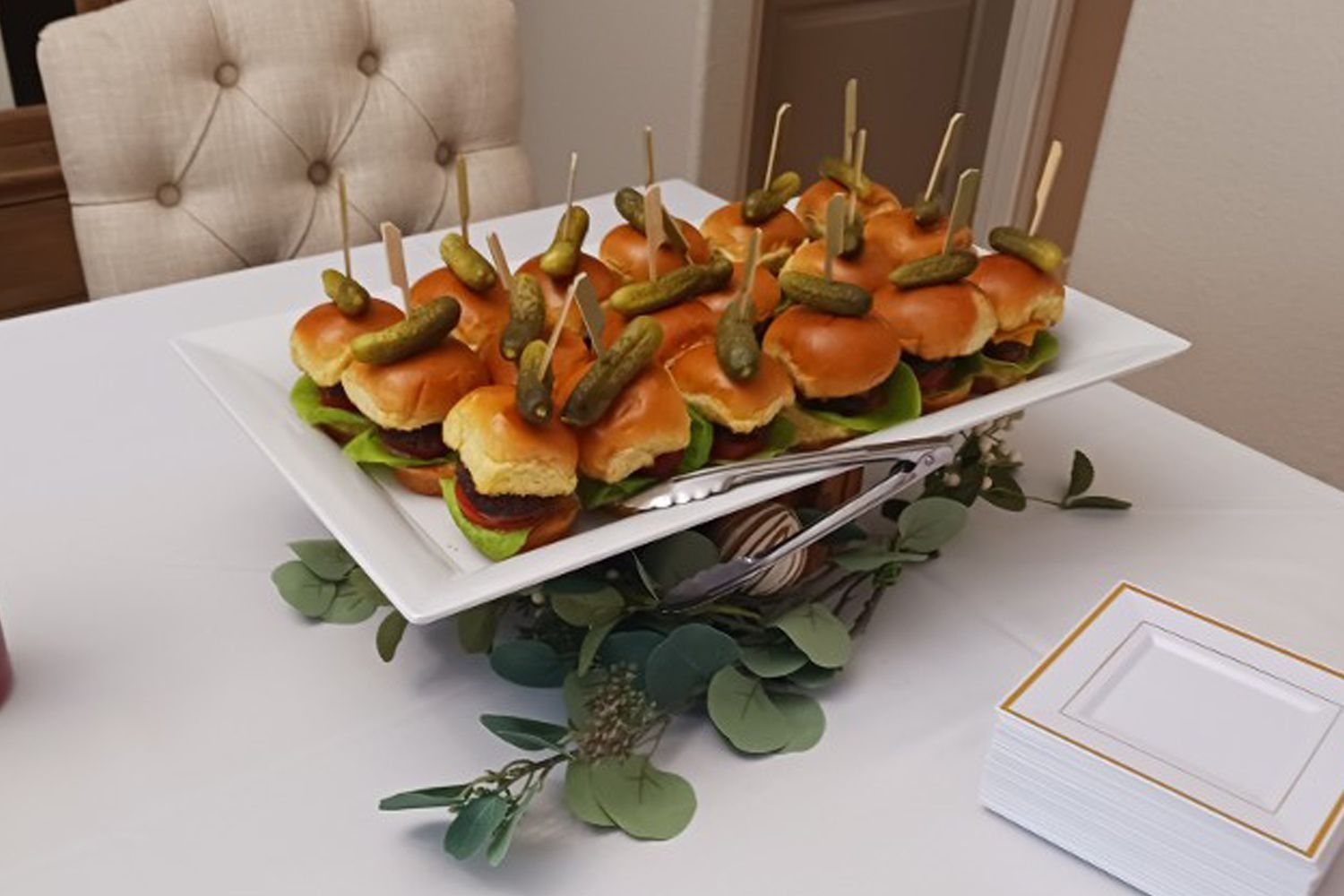 A plate of sliders with pickles on toothpicks on a table.