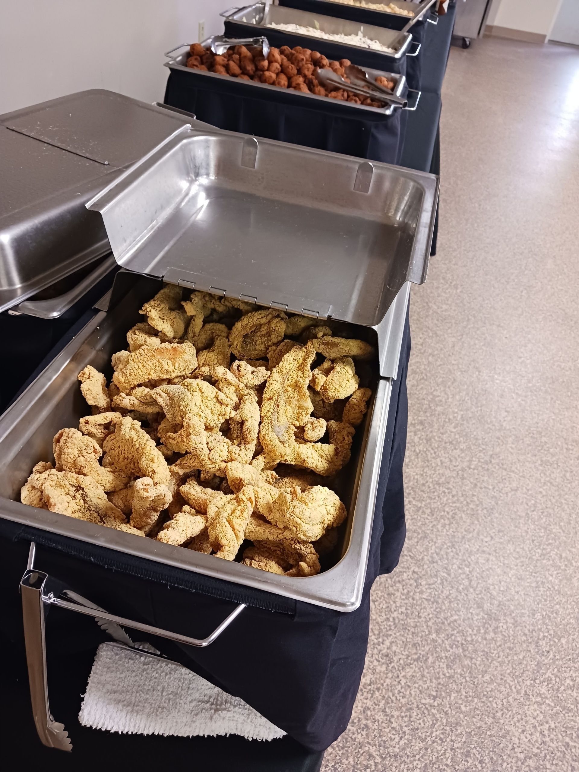 A buffet line with a tray of fried chicken on a table.