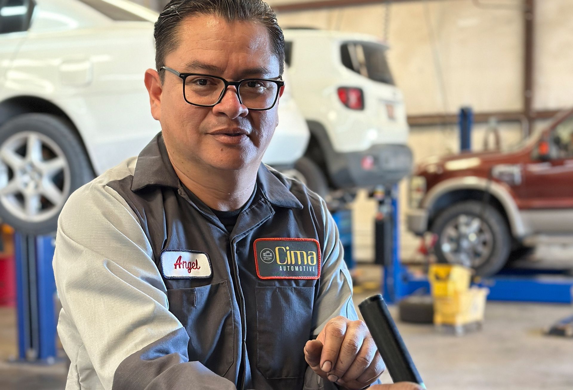 A man wearing glasses is standing in front of a car in a garage.