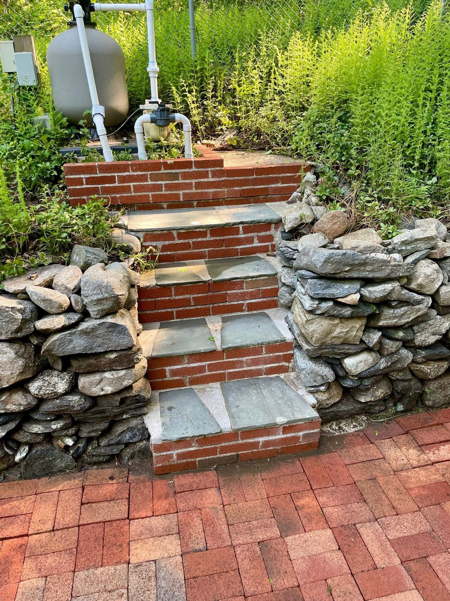 Stone garden steps with brick risers between stacked rock walls, surrounded by greenery. - after