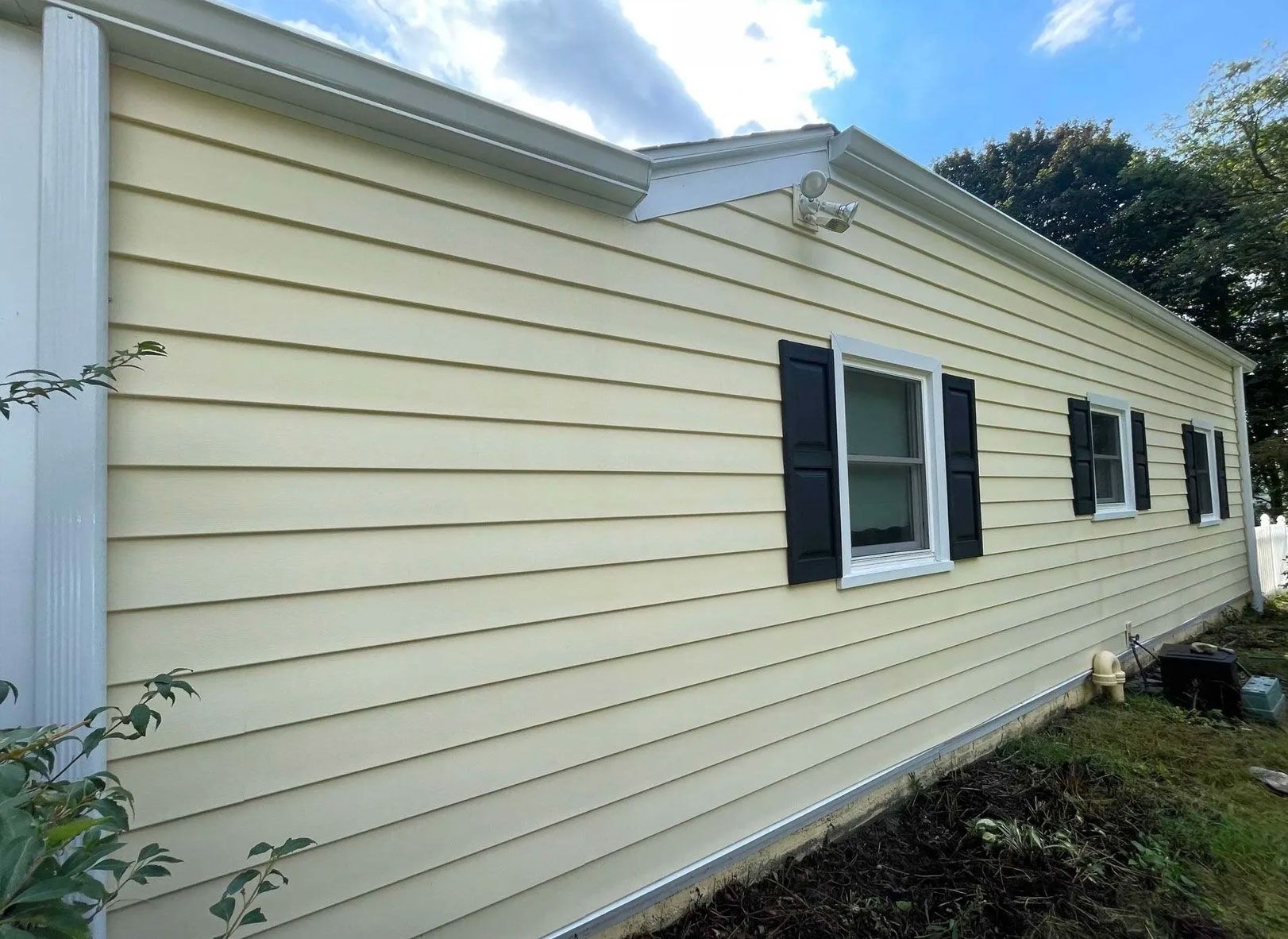 Yellow-sided house with black shutters, white trim, and a blue sky with clouds - after