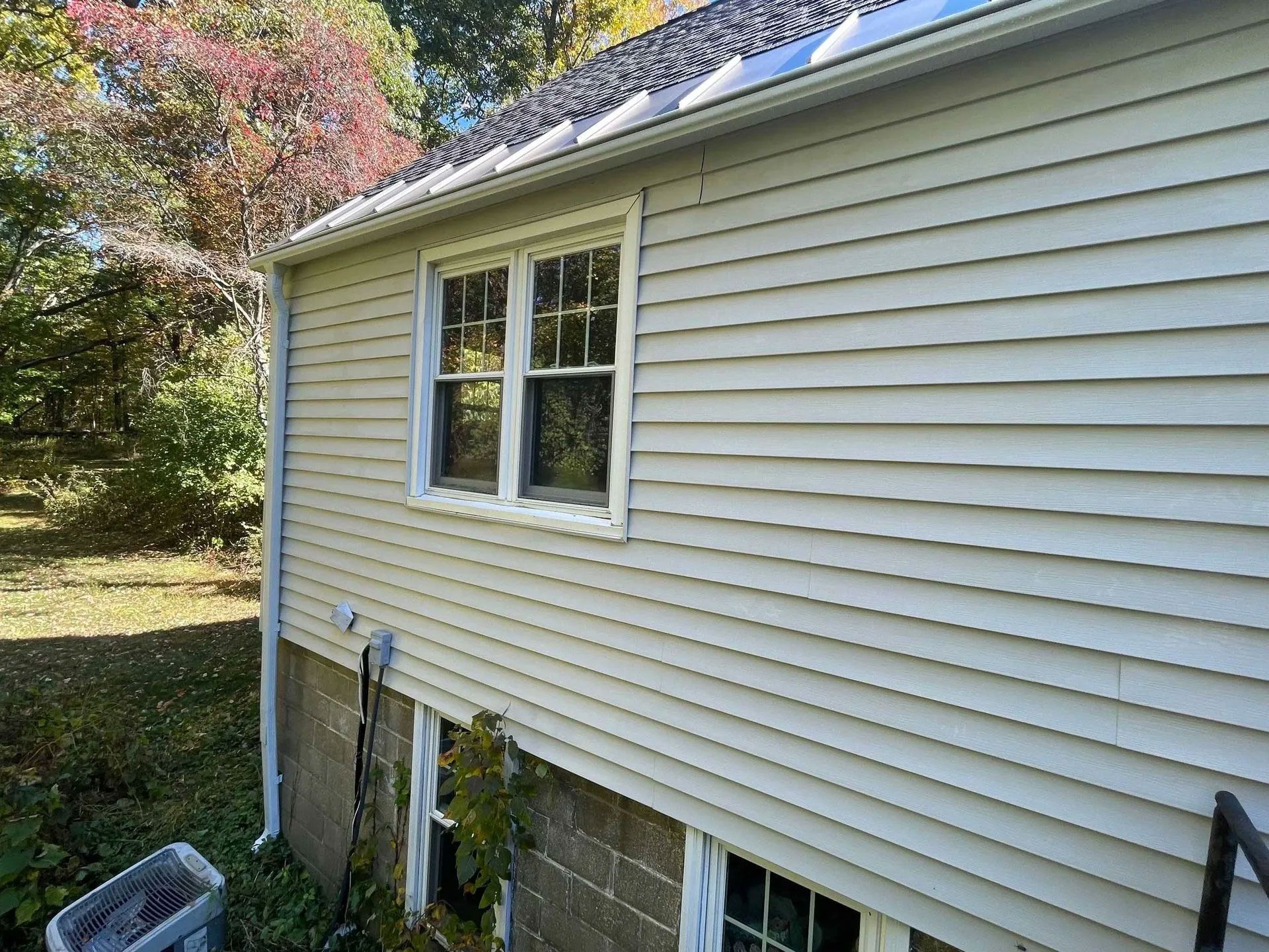Beige siding on a house with a window, door, and a partially exposed cinderblock foundation - after