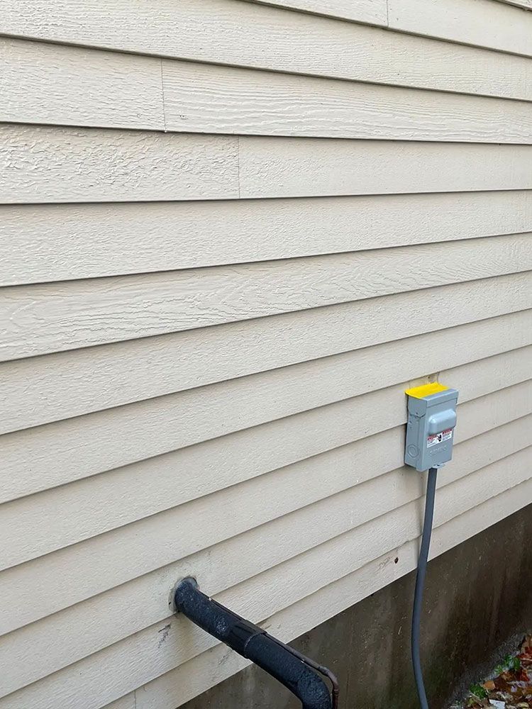 Weathered siding on a building with a utility box and black pipe extending from the wall. - after