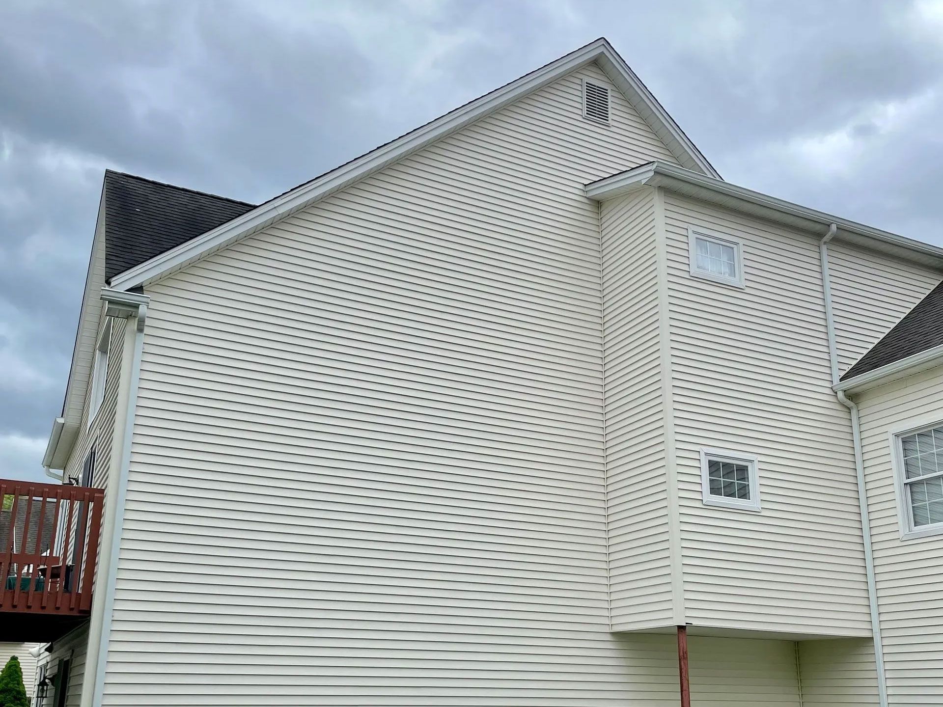 White siding on a house with significant green and brown discoloration from mildew and dirt. Cloudy outdoor setting. - after