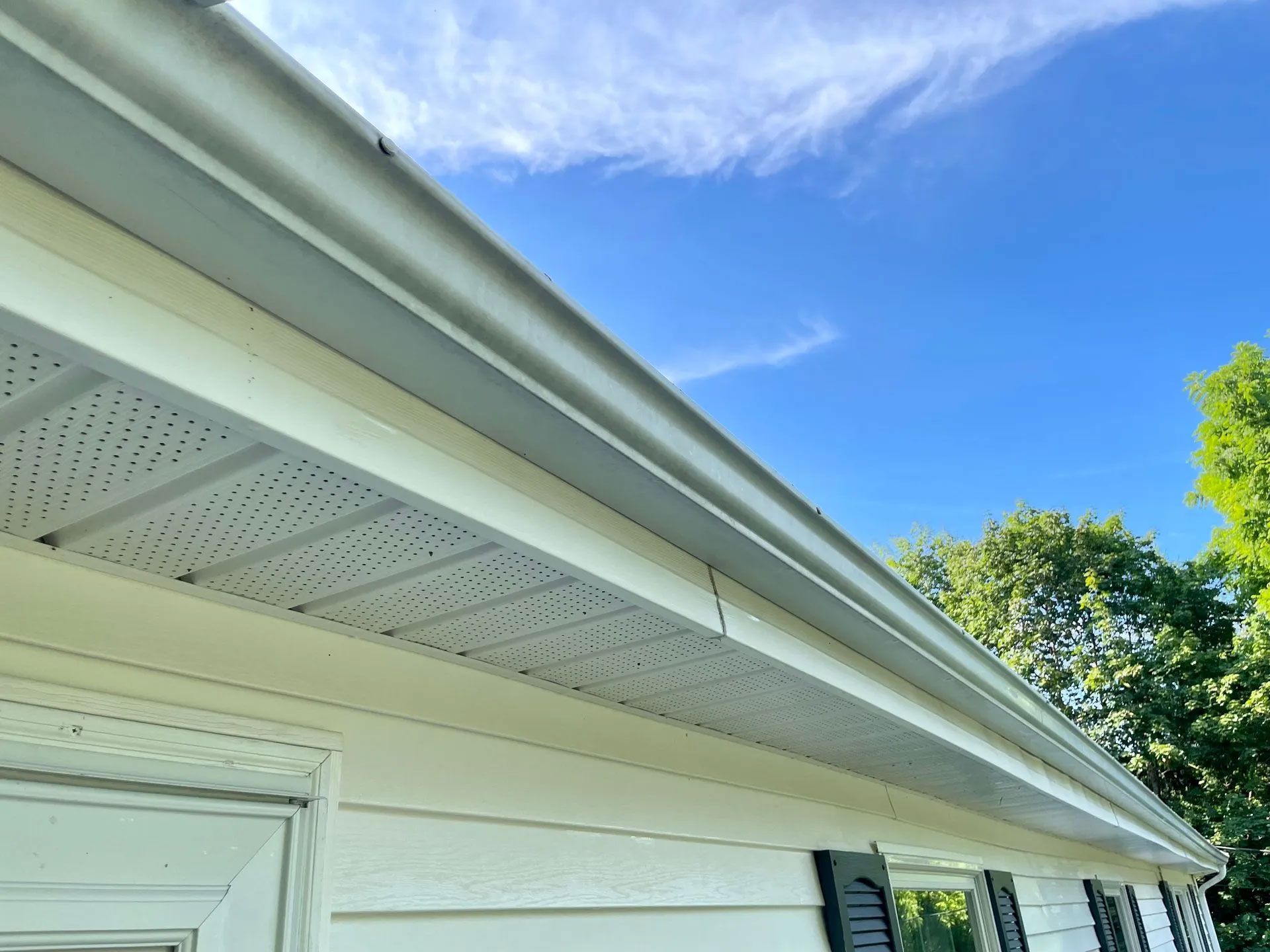 White house eaves covered in debris with perforated soffit paneling under a blue sky - after