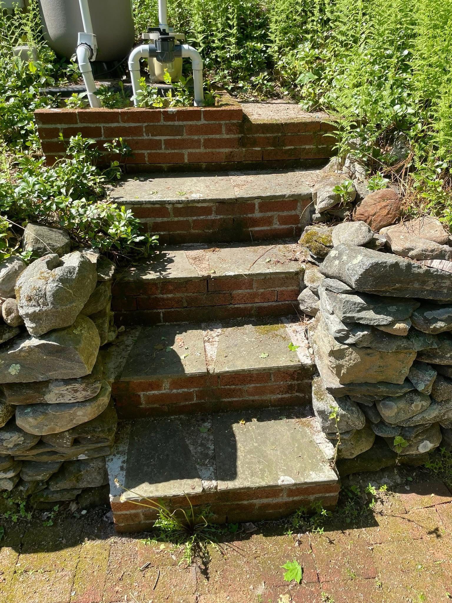 Stone garden steps with brick risers between stacked rock walls, surrounded by greenery. - before