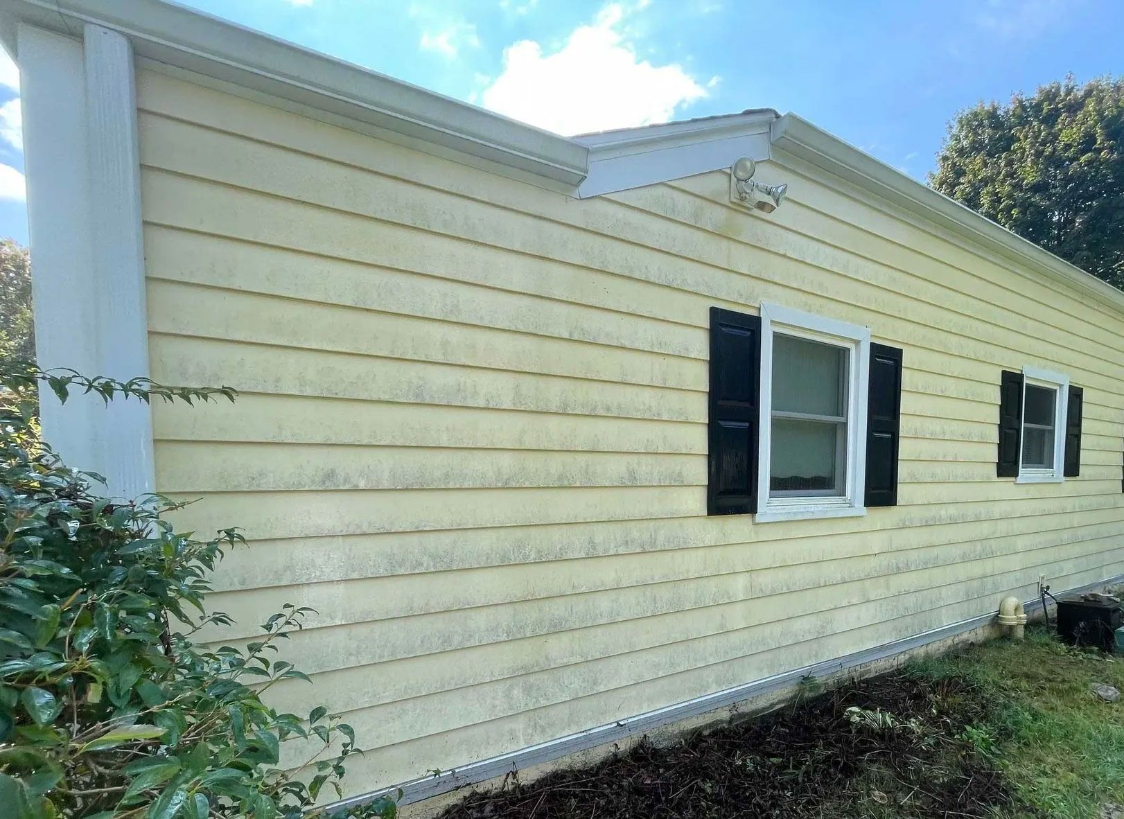 Yellow-sided house with black shutters, white trim, and a blue sky with clouds - before