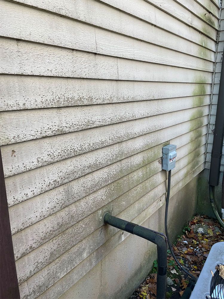 Weathered siding on a building with a utility box and black pipe extending from the wall. - before