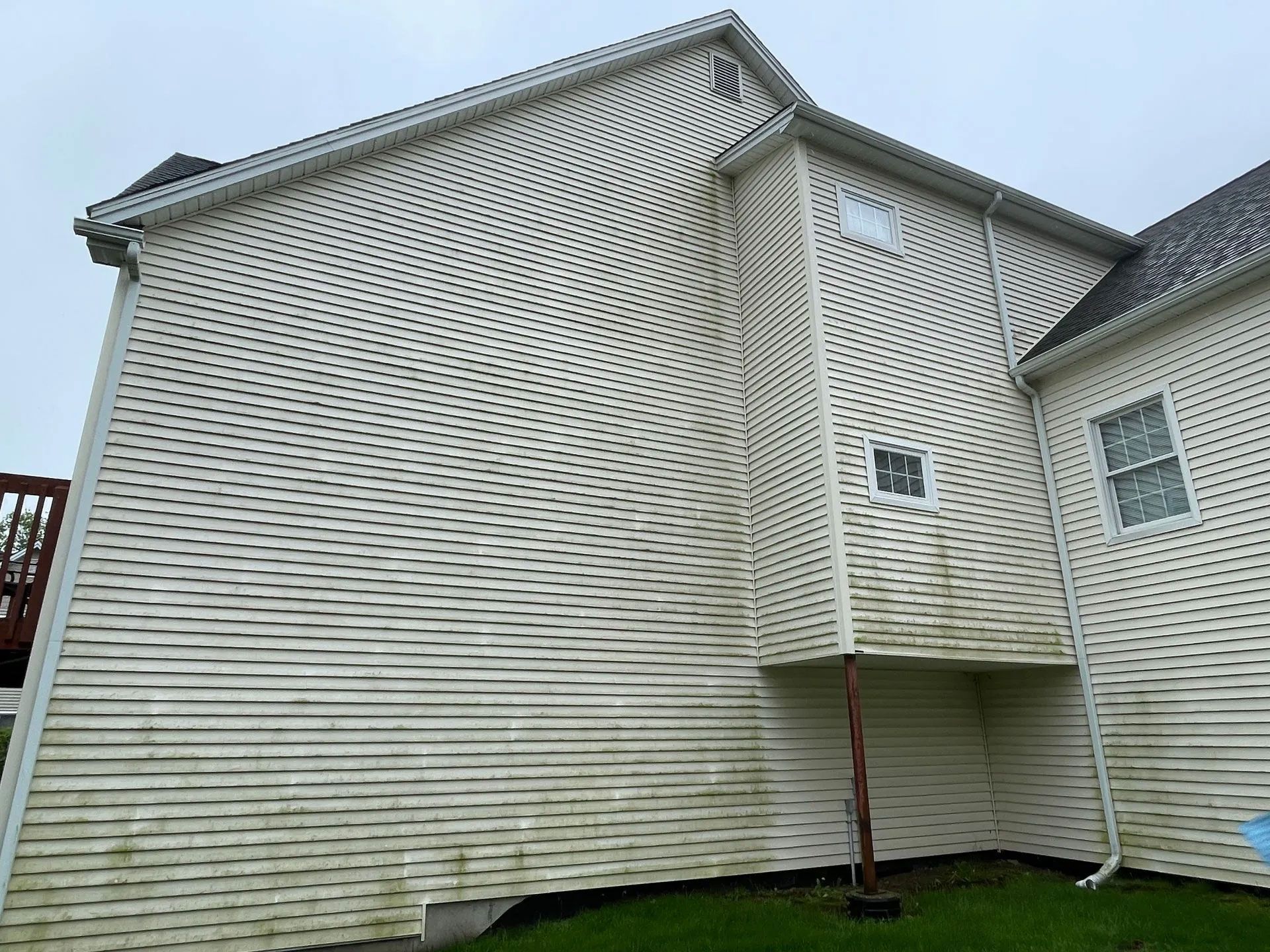 White siding on a house with significant green and brown discoloration from mildew and dirt. Cloudy outdoor setting. - before