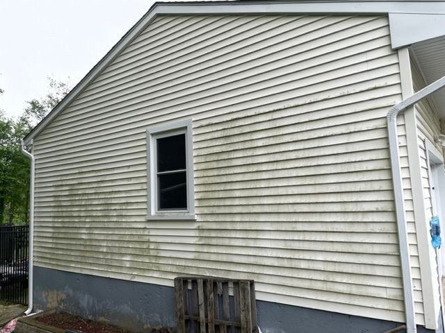A house with dirty, green siding. A window is in the center. A wooden pallet rests below. - before