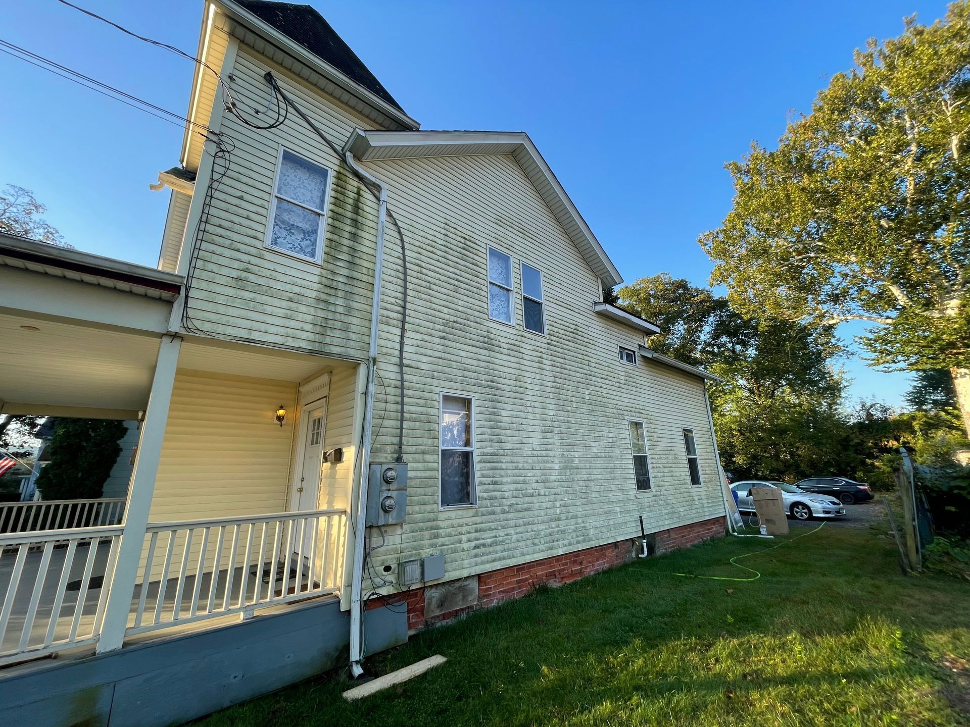 Yellow house with porch, brick foundation, and green lawn. Electrical equipment on the side. - before