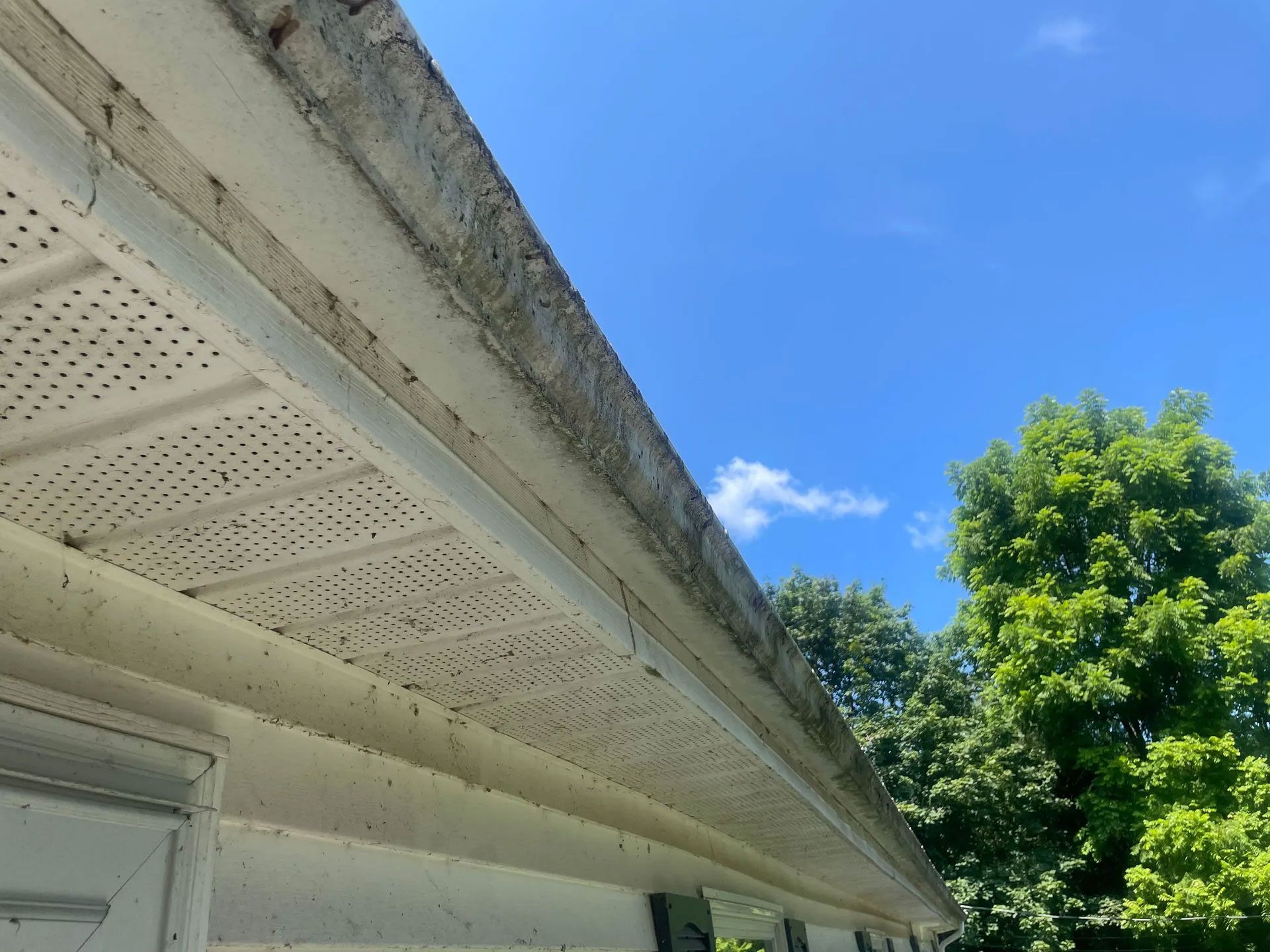 White house eaves covered in debris with perforated soffit paneling under a blue sky - before
