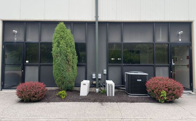 Exterior of a commercial building with dark windows, landscaping, and an HVAC unit.