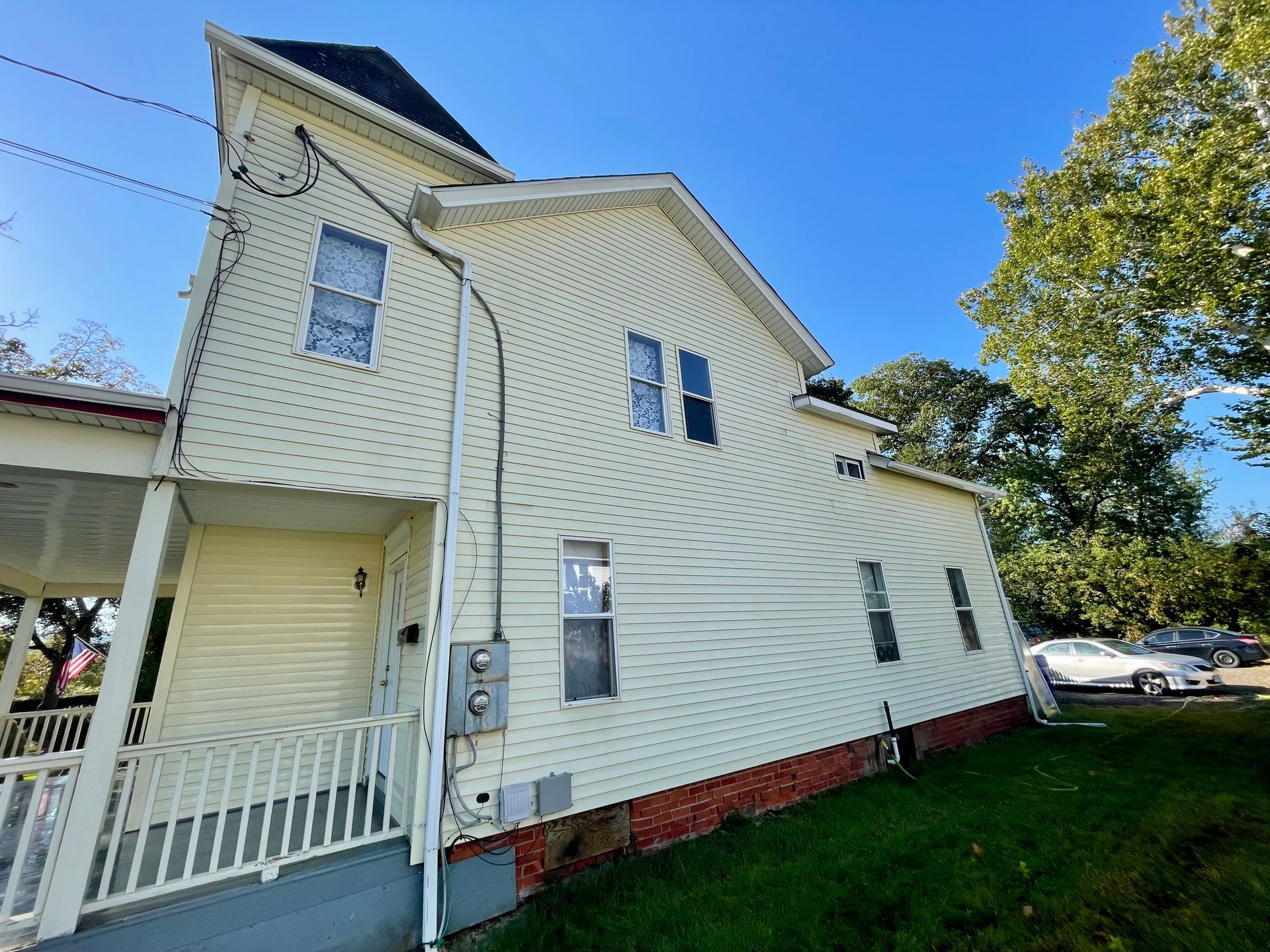 Side view of a two-story house with yellow siding, a porch, and a green lawn.
