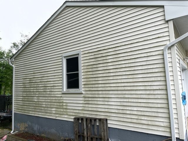 Exterior view of a house with dirty white siding and a small window; a pallet sits below the window.