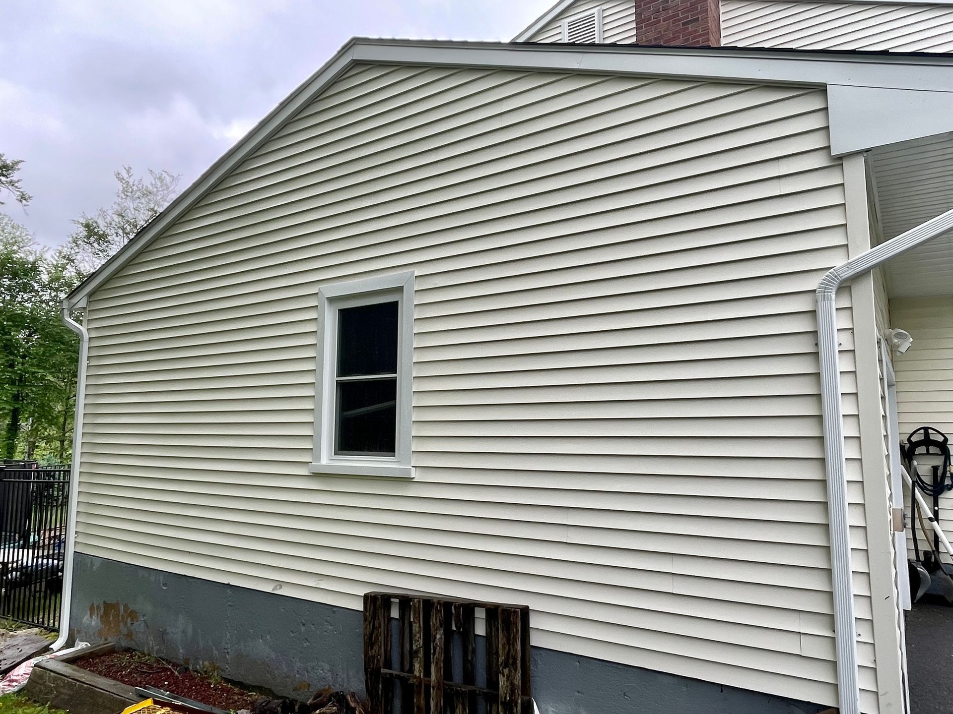 Beige vinyl-sided house with a window, white trim, and a gray foundation.