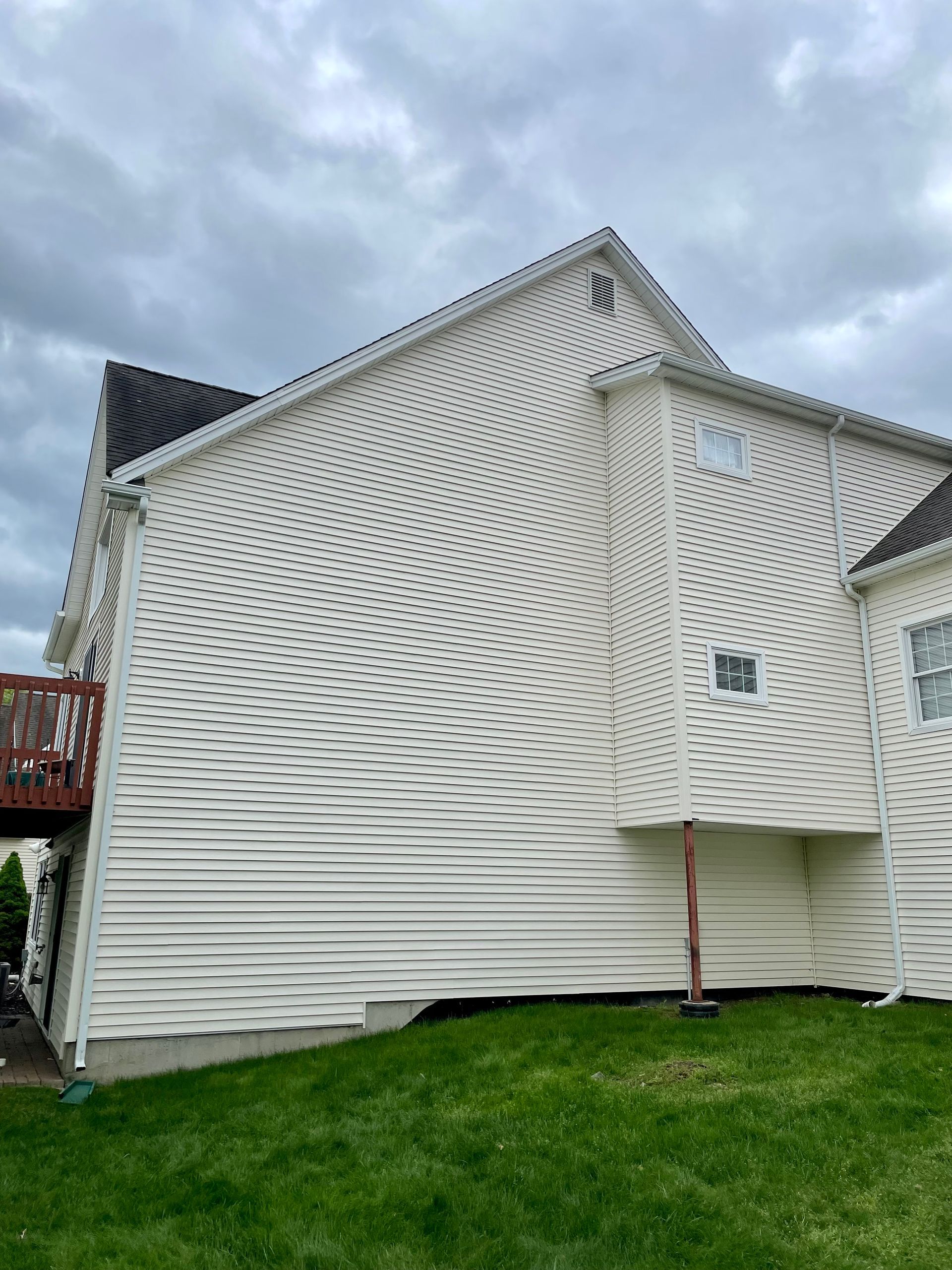 White house exterior with warped siding, under a cloudy sky, with green grass in the foreground.
